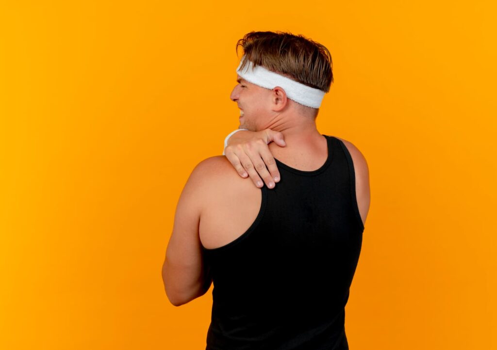 hombre sujetandose los hombros con rostro de dolor en ambiente interior luminoso