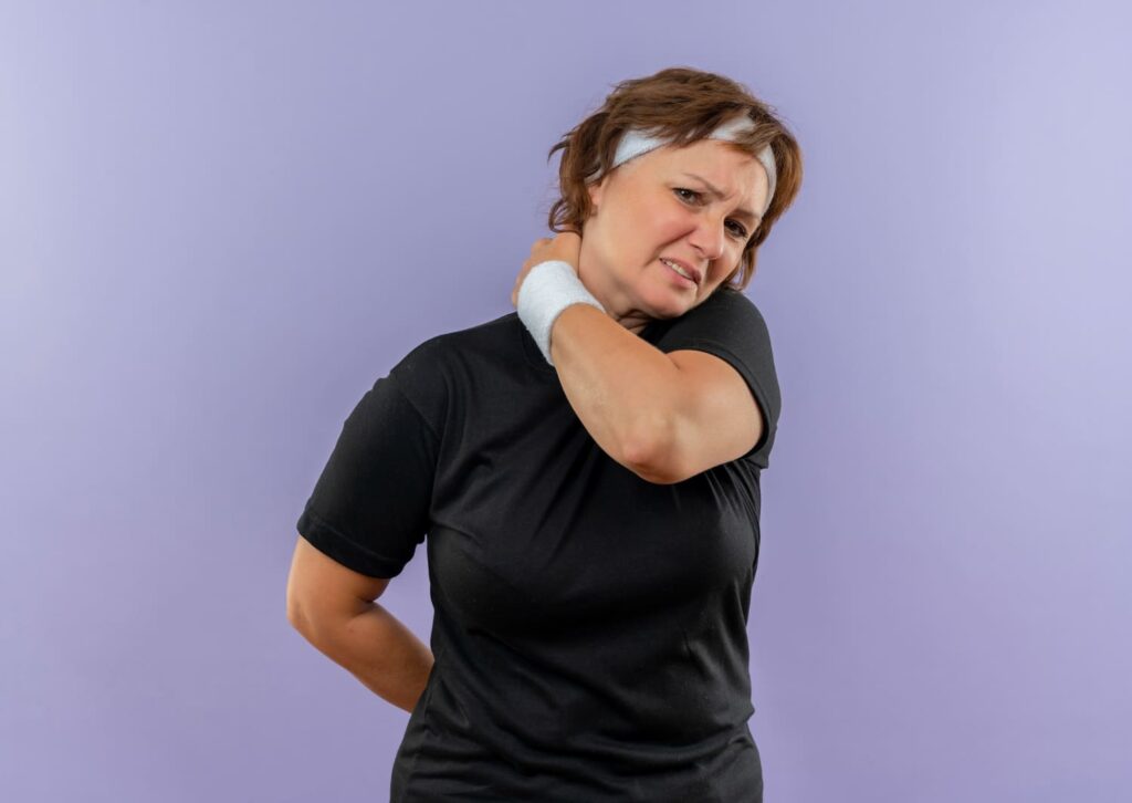 mujer con dolor en cuello sujetandose con mano en fondo lila liso