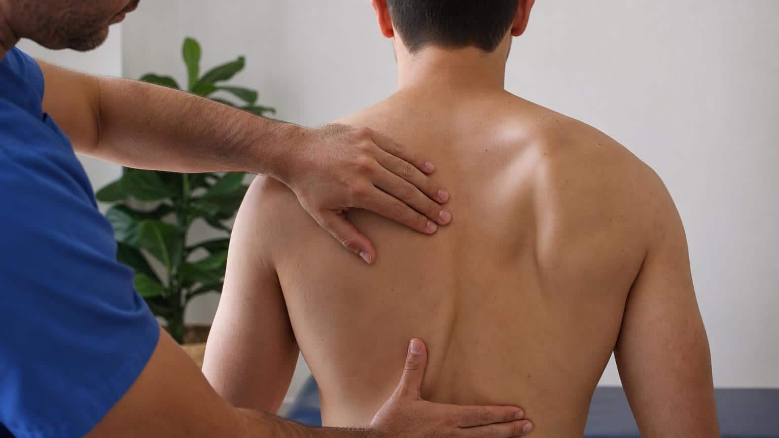 Physiotherapist examining a man's back, showing a protruding right shoulder blade characteristic of winged scapula.